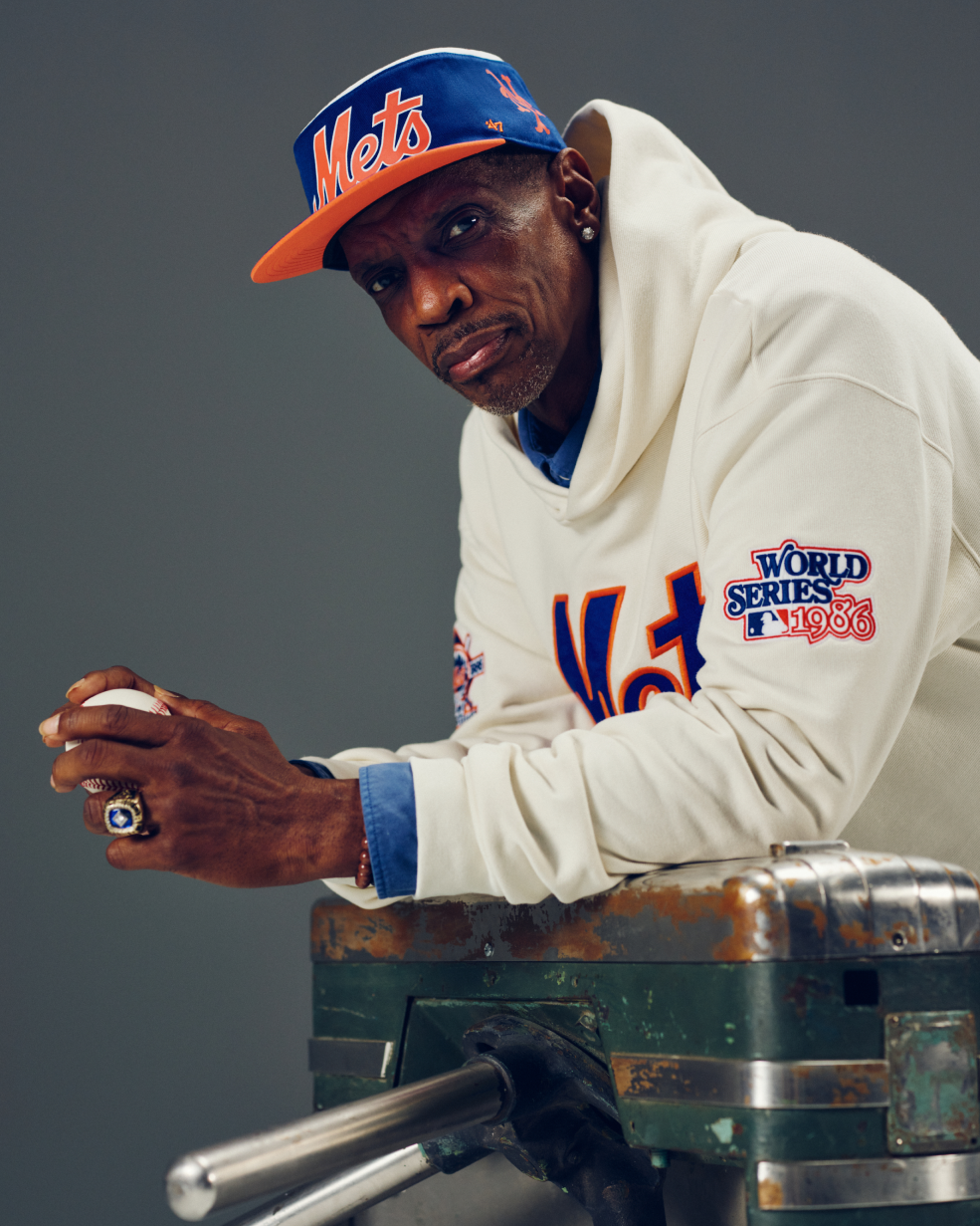 Person wearing a Mets cap and hoodie with a World Series patch, holding a baseball.