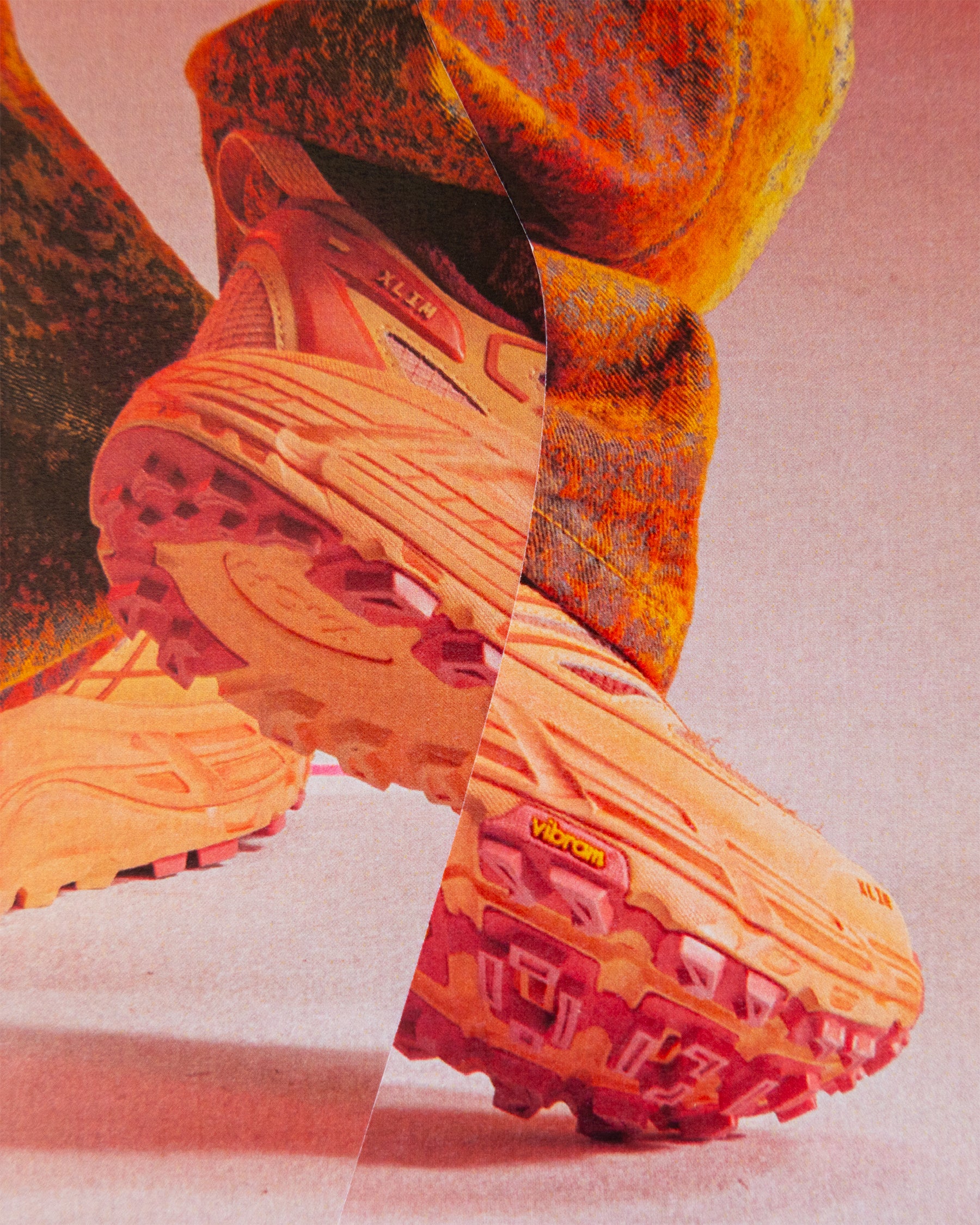 Close-up of orange and red hiking boots with a brand logo on a pink background